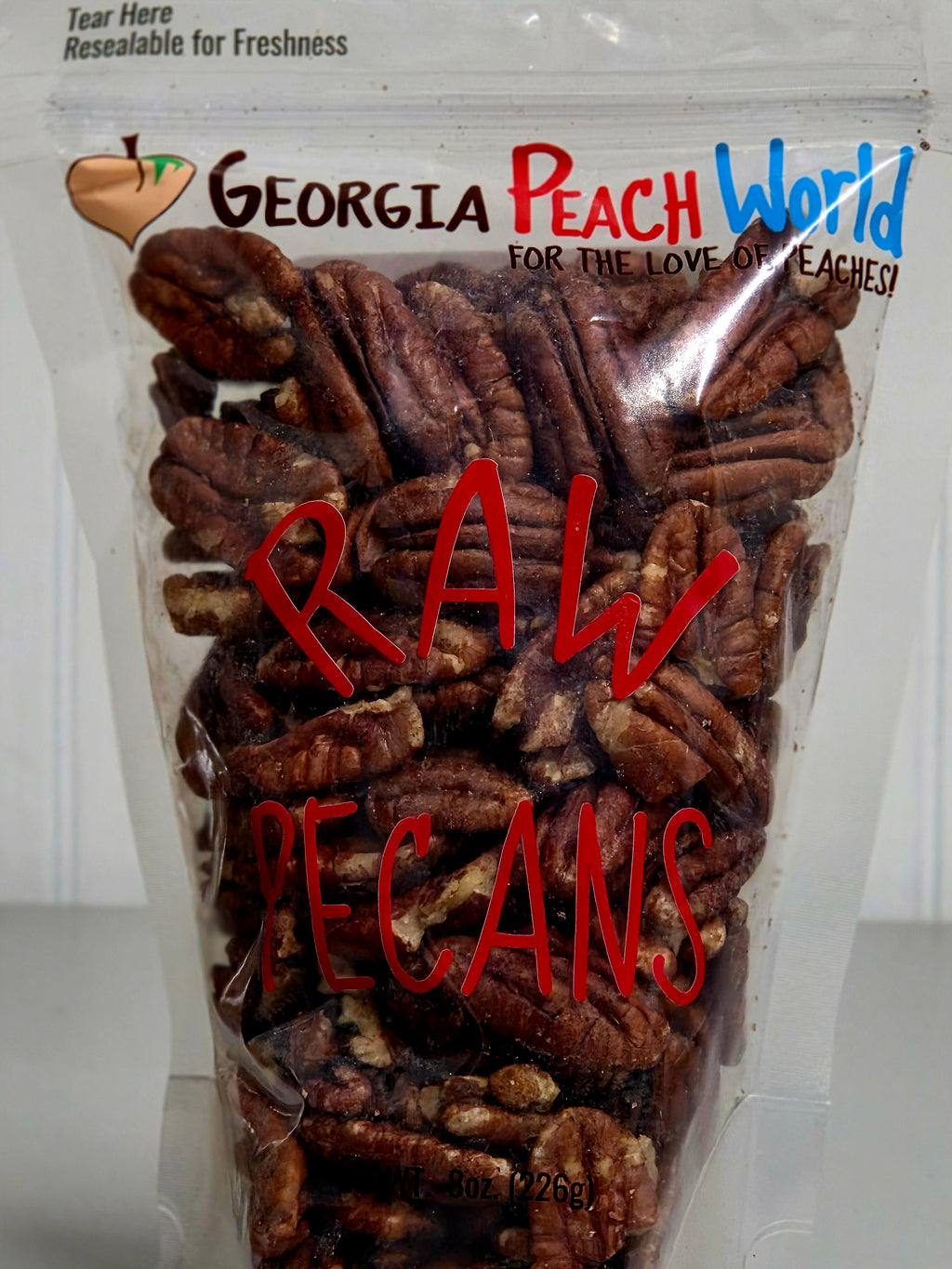 Bag of raw pecans with 'Georgia Peach World' branding on a white background