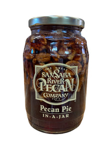 Large glass jar containing pecans suspended in a dark syrup blend.