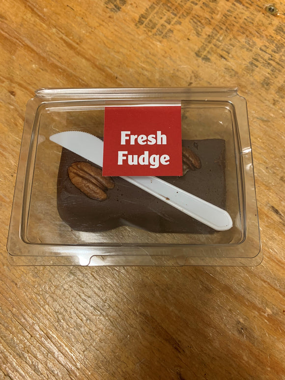 Small plastic hinged clamshell containing a block of chocolate fudge topped with pecans