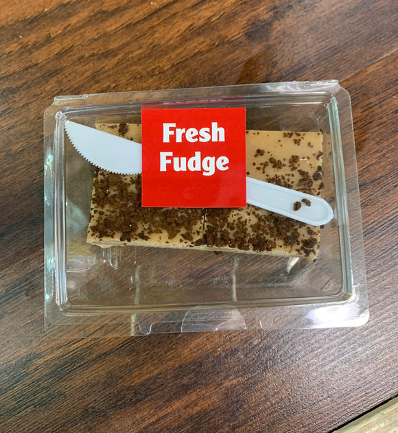 Plastic hinged clam shell containing a block of peanut butter flavored fudge. Small plastic knife is included in the container.